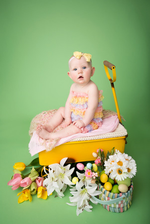 Baby girl in Easter outfit with Easter Eggs, and tulip flowers, sitting in a yellow cartの写真素材