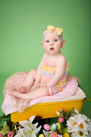 Baby girl in Easter outfit with Easter Eggs, and tulip flowers, sitting on blanketの写真素材