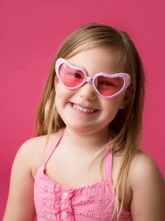 Happy smiling girl in heart shaped pink glasses looking at cameraの写真素材