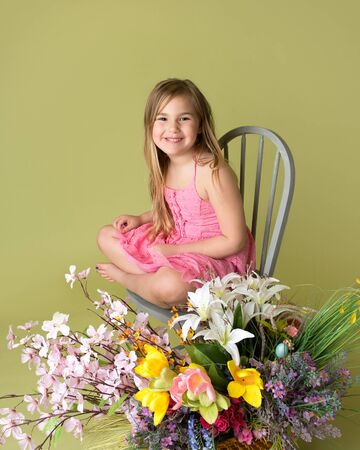 Happy smiling girl with a bunch of spring flowers in a basket looking at the camera, green backgroundの写真素材