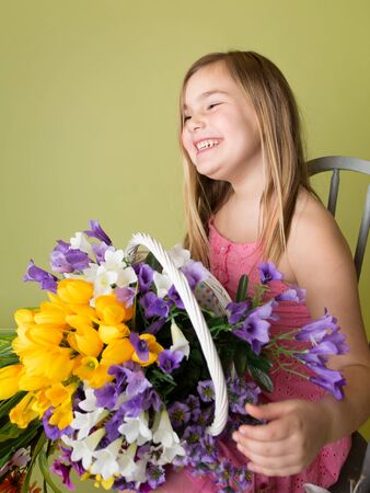Happy smiling girl with a bunch of spring flowers in a basket looking at the camera, green backgroundの写真素材