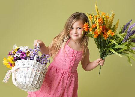 Happy smiling girl with a bunch of spring flowers in a basket looking at the camera, green backgroundの写真素材