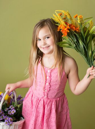 Happy smiling girl with a bunch of spring flowers in a basket looking at the camera, green backgroundの写真素材