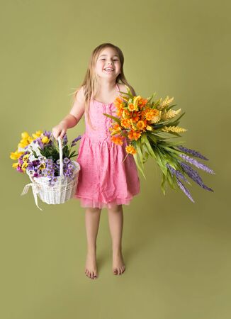 Smiling girl standing with a basket of spring flowers looking at the camera, green backgroundの写真素材
