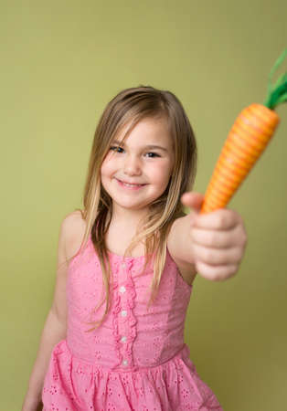 Happy smiling girl holding a carrot, for feeding Easter Bunny, spring, seasonal themeの写真素材