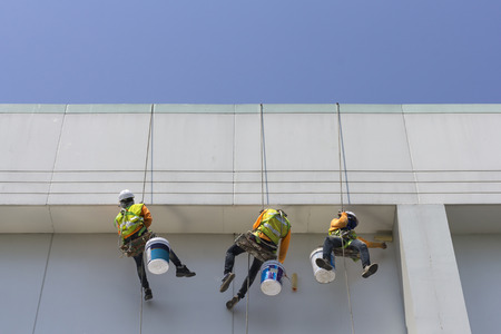 Painters and harnesses hanging high building