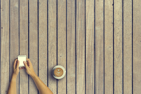 Top view of Business people using a smartphone with a cup of latte coffee on old wooden desk background.Vintage tone and Copy space.の写真素材