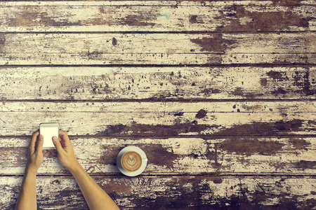 Top view of Business people using a smartphone with a cup of latte coffee on old wooden desk background.Vintage tone and Copy space.の写真素材