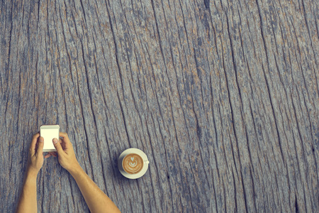 Top view of Business people using a smartphone with a cup of latte coffee on old wooden desk background.Vintage tone and Copy space.の写真素材