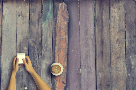 Top view of Business people using a smartphone with a cup of latte coffee on old wooden desk background.Vintage tone and Copy space.の写真素材