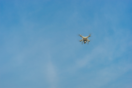 White drone hovering in a bright blue sky and clouds