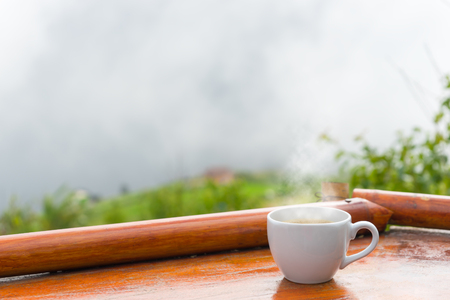A cup of coffee put on old wooden table with view of Morning fogの写真素材