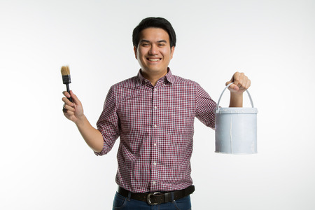 Portrait of young asian handsome smiling painter holding paintbrush and paint bucket on white background.の写真素材