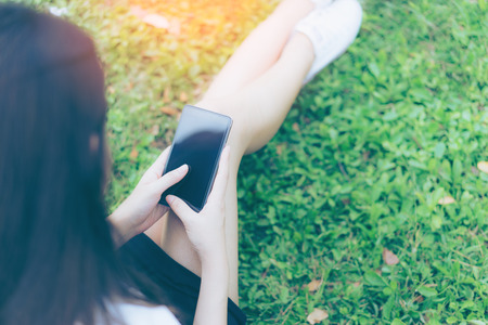 Beautiful Young asian woman using smartphone in garden. Portrait of asian women reading message with smart phone in park outdoor. の写真素材