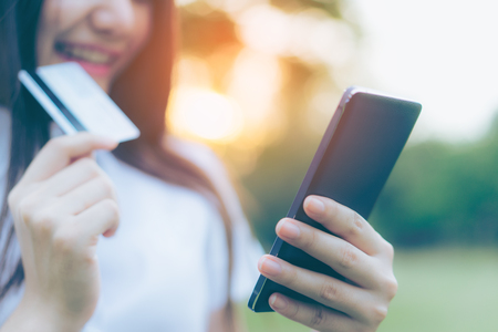 Beautiful Young asian woman smiling while using her smartphone to shop online with credit card in garden background. Portrait of asian women shopping by creditcard with smart phone in park outdoor. の写真素材