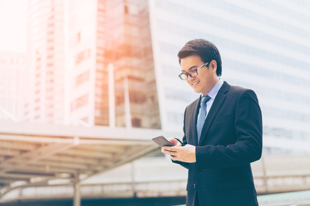 Young asian handsome businessman and glasses using smartphone with smiling at business districtの写真素材