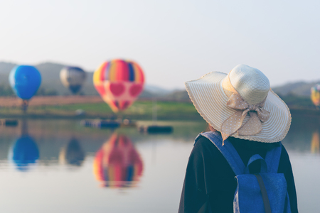 Woman tourist is traveling into Balloon festival in Chiangrai Provice, Thailand. Woman traveller with white hat and bag standing looking beautiful balloon lake.の写真素材