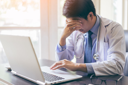 Portrait of a young handsome doctor using his laptop computer with seriousの写真素材