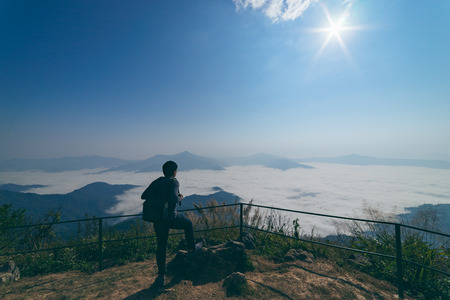 Man tourist is traveling into the peak of mountain and cloudscape at Doi Pha Tang in Chiangrai Thailand. Man traveler with bag standing looking beautiful mist at sunrise. Hiking trekking conceptの写真素材