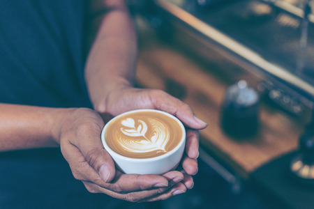 Man hands holding fresh coffee or latte art in white cup at coffee shop and restaurant, bar or pub.の写真素材