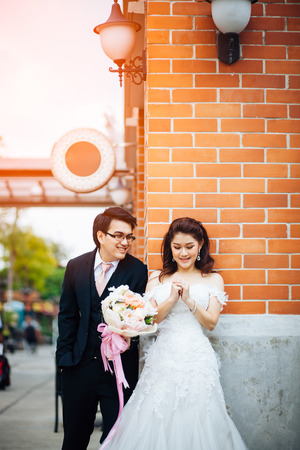 The bride and groom smiling together and give flowers in old town background. Asian wedding couple  smiling together and give flowers in old town background.の写真素材