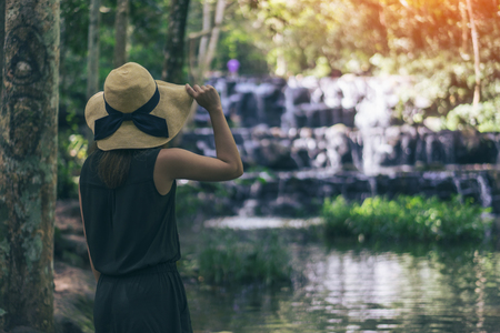 Young woman traveler and freedom. Young woman in hat with rucksack enjoying tropical waterfall view.の写真素材