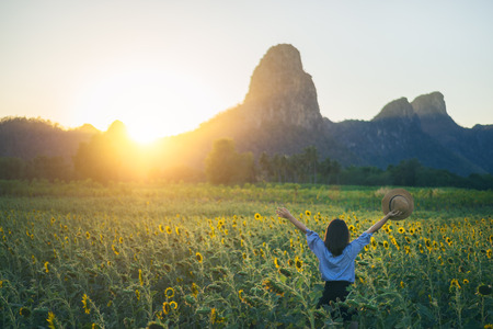 Young woman traveler with hat in sunflower fields with happiness and cheerful at sunset and arms raised up.の写真素材