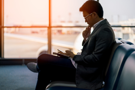Young asian businessman sitting and using smartphone at waiting area in international airportの写真素材