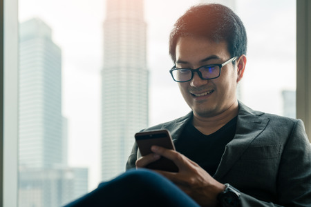 Young asian businessman using smartphone with happiness in hotel with background of cityscape in...