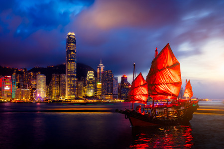 Hong Kong City skyline with tourist sailboat at night. View from across Victoria Harbor Hong Kong.の写真素材