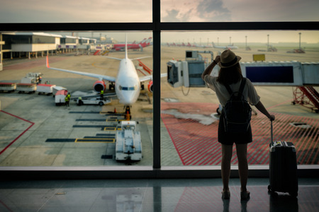 Young asian woman with baggage looking through the window of an airport departure loungeの写真素材