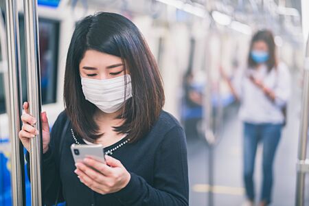 Young asian woman wearing protective face mask using smartphone in underground train due to the...