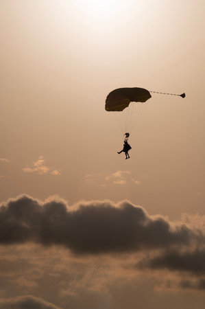 Vertical image of a silhouette of a tandem of parachuters with some dark clouds as backgroundの写真素材