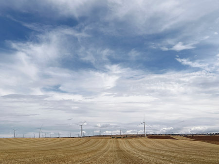 Wind turbines stand on a harvested field, capturing clean energy under an expansive cloudy sky in Atalaya del Canavateの写真素材