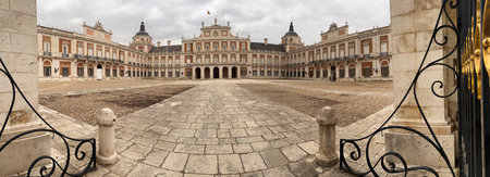 The Royal Palace of Aranjuez displaying its magnificent architecture and vast Plaza de Armas under a cloudy skyの写真素材