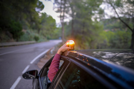 Person placing emergency warning beacon V16 on car roof during roadside breakdown for safetyの写真素材