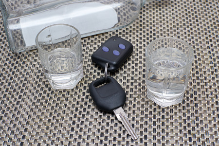 car keys on the table next to full glasses of alcohol and empty a bottle of vodkaの写真素材