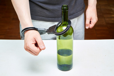 Man in handcuffs interconnected with a bottle of wineの写真素材