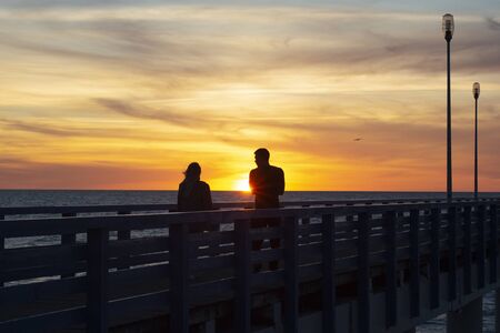 Two young lovers standing on a promenade and look on the sea. Beautiful sunset on the sea.の写真素材