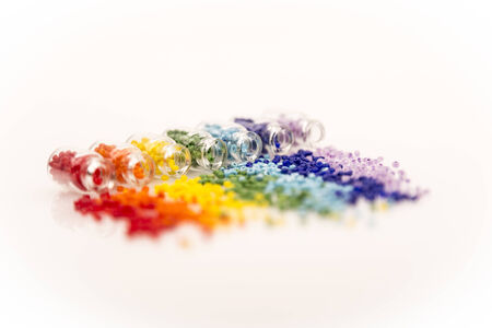 Selective focus tiny glass bottles filled with a rainbow colours of beads spilling out, on a white...