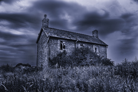 Spooky, haunted, derelict house with broken windows under a stormy sky. Black and white with a blue tint effect.の写真素材