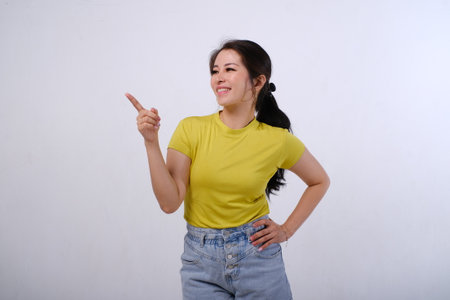 Photo of happy beautiful Asian women wear colorful shirt pointing fingers left, showing info on empty space or copy space for product isolated on white backgroundの写真素材