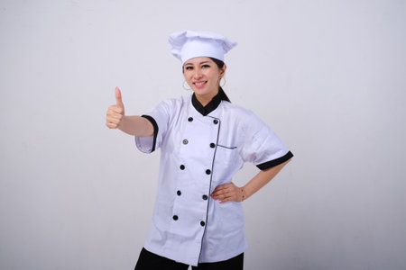 Photo of smiling female Asian chef standing showing thumb up like gesture of approval on isolated white backgroundの写真素材