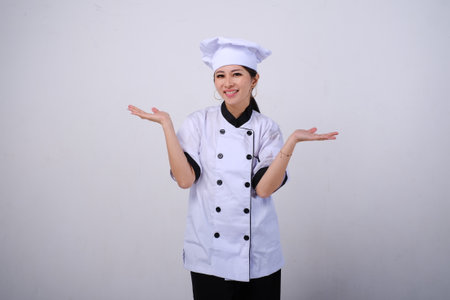 Photo of smiling female Asian chef standing with open palms, warm welcome gesture on empty space or copy space for product isolated on white backgroundの写真素材