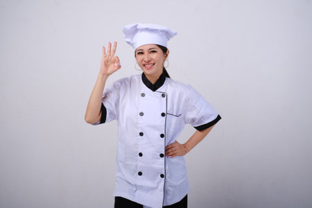 Photo of smiling female Asian chef standing showing OK hand sign gesture of approval on isolated white backgroundの写真素材