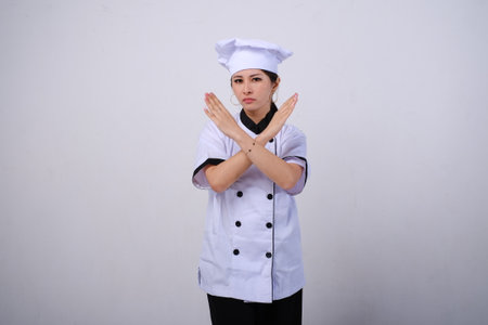 Photo of disappointed female Asian chef standing with crossed arms gesture, giving warn to stop, rejection concept on empty space or copy space on white backgroundの写真素材