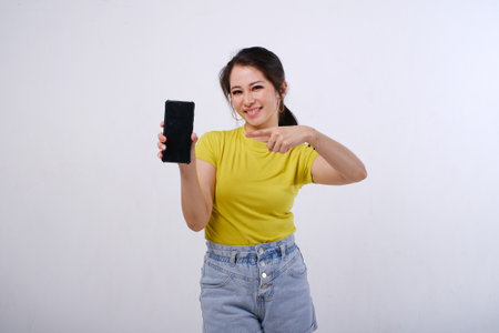 Photo of smiling female Asian showing mobile phone screen with hands pointing at blank phone screen on isolated white backgroundの写真素材