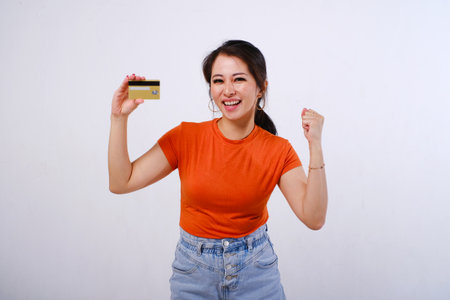 Excited and happy Asian woman wearing casualÂ shirt holding credit card isolated on white backgroundの写真素材