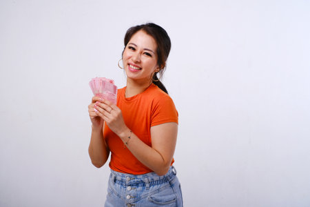 Smiling Asian woman wearing casualÂ shirt holding Indonesian money isolated on white backgroundの写真素材