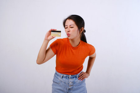 Excited and happy Asian woman wearing casualÂ shirt holding credit card isolated on white backgroundの写真素材